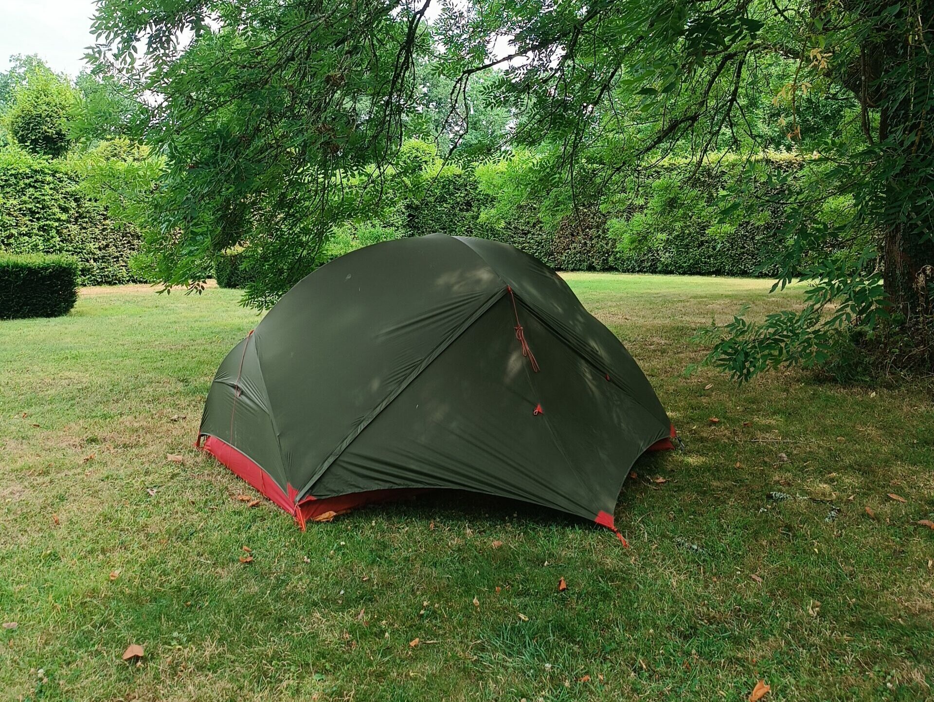 Emplacement de bivouac ombragé pour tente dans le jardin Tente de randonnée installée à l'ombre d'un grand arbre sur une pelouse verte au Manoir de Kerledan.