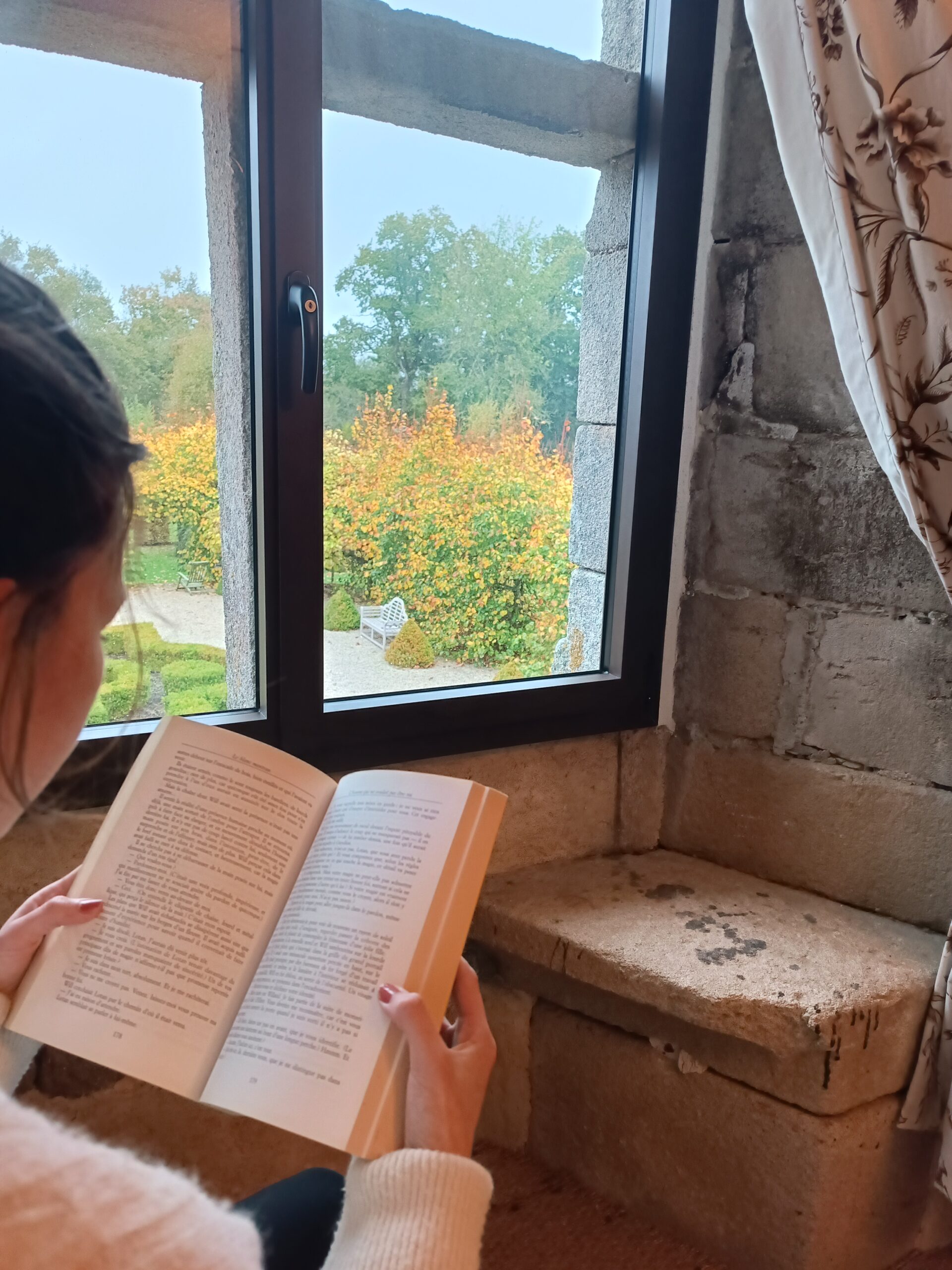 Lecture au calme - Séjour cocooning en Bretagne Femme lisant un livre au coin de la fenêtre avec vue sur le parc en automne au Manoir de Kerledan